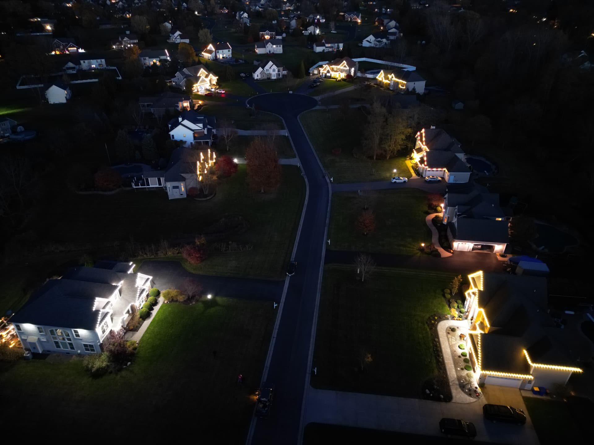 Aerial night view of a Rochester NY neighborhood with several homes lit by professional Christmas lighting