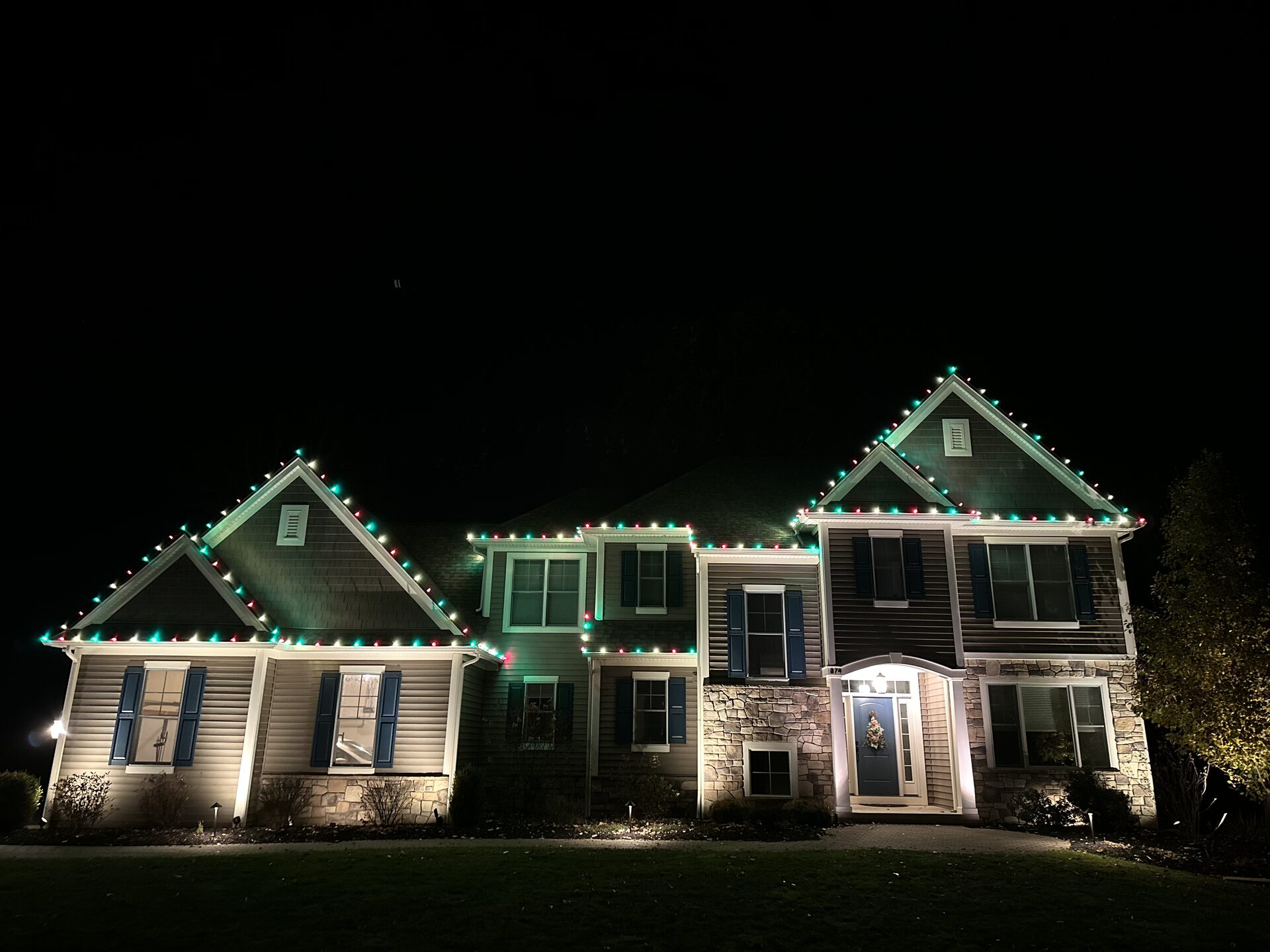 Red, green and white custom-cut Christmas lights outlining the peaks of a Rochester NY home at night